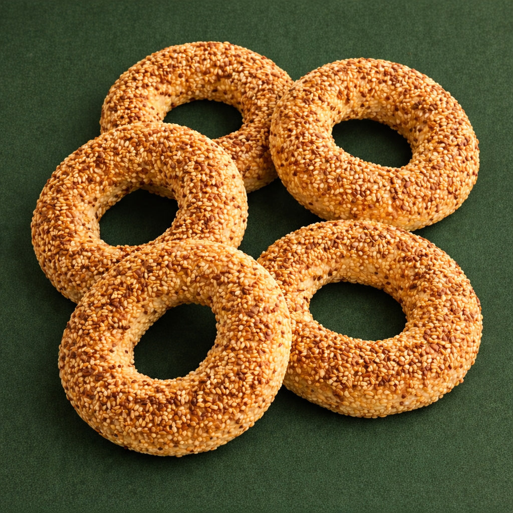 Draufsicht auf fünf goldbraun gebackene, ringförmige Sesamgebäcke (Simit) auf dunkelgrünem, cleanem Hintergrund in Etikettfarbe, ohne weitere Deko.