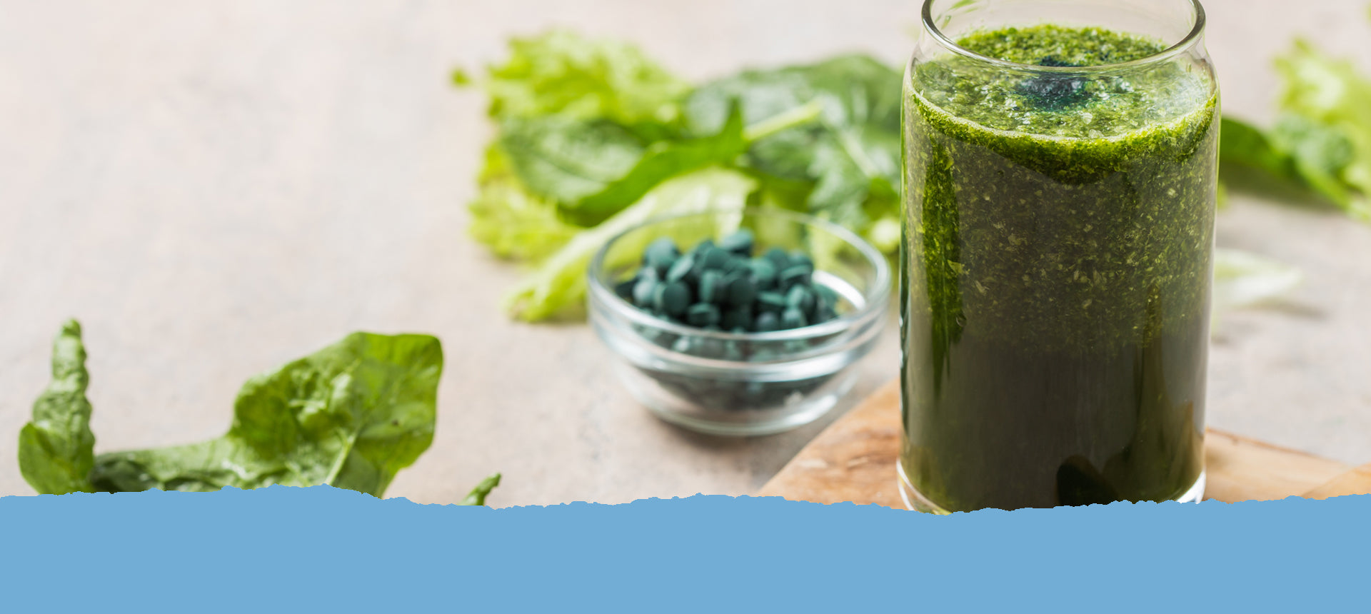 Ein grüner Smoothie mit Spirulina, daneben ein Glas-Schälchen mit grünen Presslingen. Dahinter liegen Blätter von Chlorella und Spirulina. Text: Unsere Kapseln und Presslinge