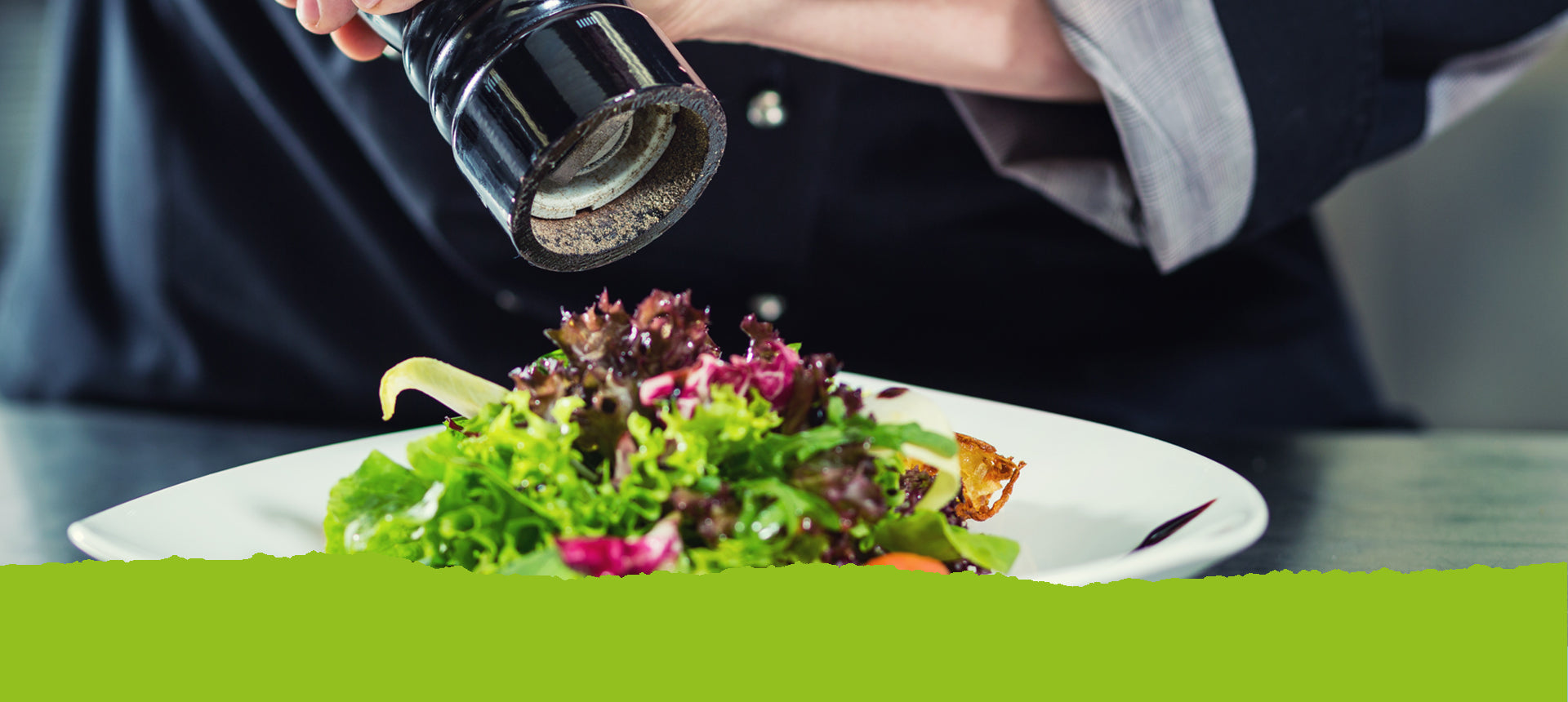 Eine Person dreht an einer Pfeffermühle über einem bunten Salatteller. Text: Unser Pfeffer und Salz