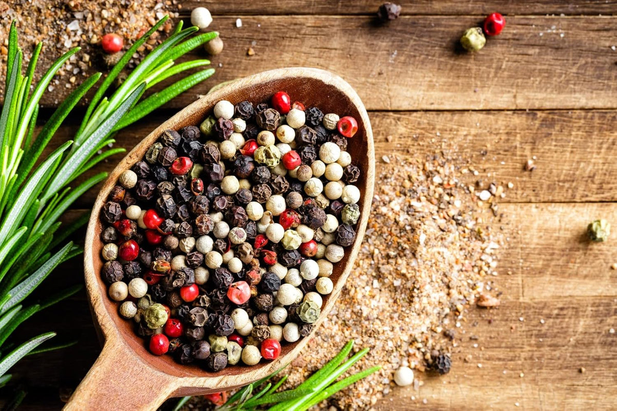 Bunter Pfeffer ganz als Zutatenmotiv für JKR Spices Bratkartoffel Gewürzmischung, Pfefferkörner im Holzlöffel auf rustikalem Holztisch mit Rosmarin
