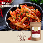 Eine Pfanne mit Penne und gebratenen Tomaten, davor eine Packung mit Chili Flocken. Text: Für die besondere Note