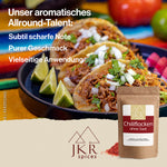 Eine bunte Tischdecke, darauf ein Teller mit gefüllten Tortillas und geviertelten Limetten. Text: Subtil scharfe Note/Purer Geschmack/Vielseitige Anwendung