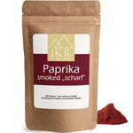 JKR Spices Paprika Smoked „Scharf“ im braunen Doypack, geräuchertes Paprikapulver als roter Gewürzhaufen vor weißem Hintergrund