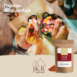 Hände, die einen Tortilla-Wrap belegen, davor eine Packung mit Chili Flocken. Text: Für einen würzigen Kick