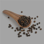 Ganze schwarze Pfefferkörner in Holzlöffel mit verstreuten Pfefferkörnern auf grauem Hintergrund